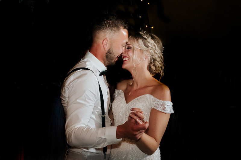 Newly wed husband and wife, embrace closely whilst performing their first dance.  she smiles as she looks into his eyes.